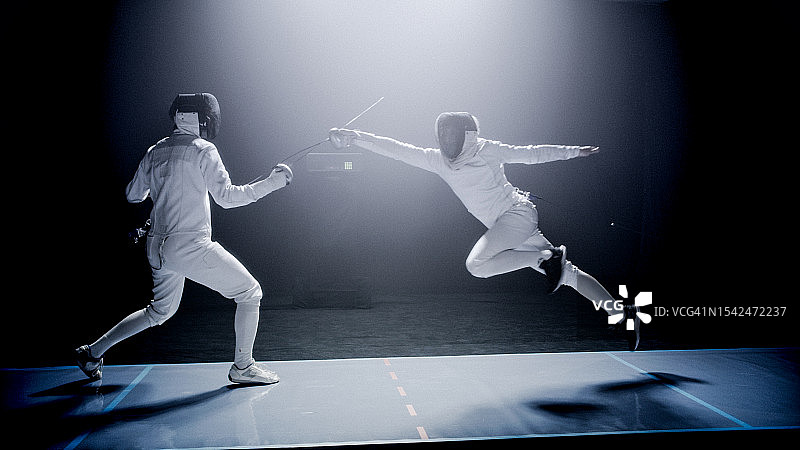 两位专业击剑手在史诗般的蓝色舞台灯光和烟雾效果下进行花剑决斗图片素材