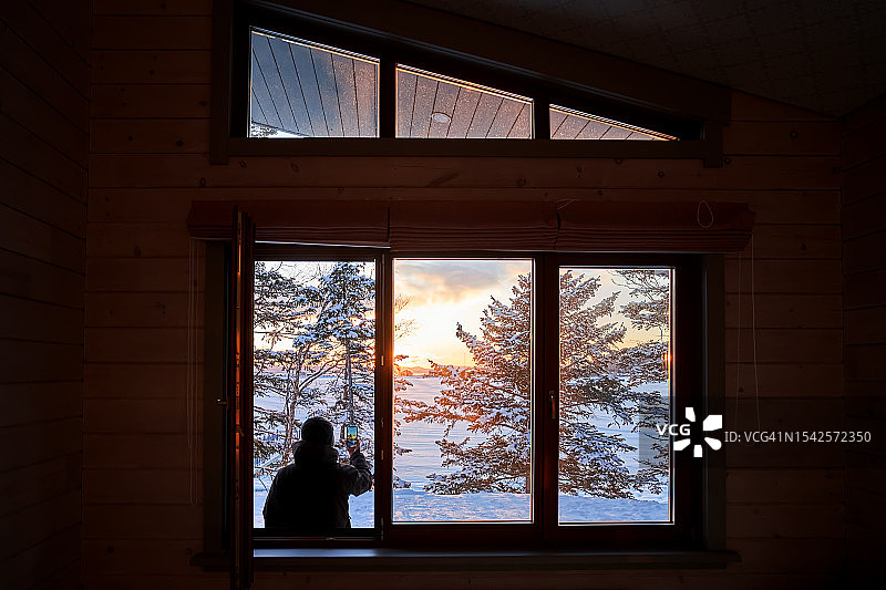 男子站在窗外，以雪景为背景用手机拍照图片素材