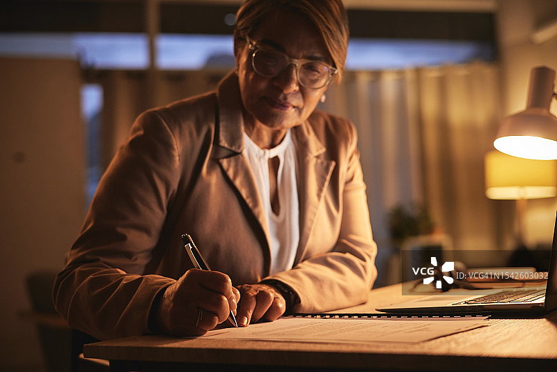 中年妇女在公司和夜晚，撰写报告，办公室里的文书工作和律师正在进行案例研究。女律师，工作效率和加班，办公桌上的法律文件或文件夹图片素材