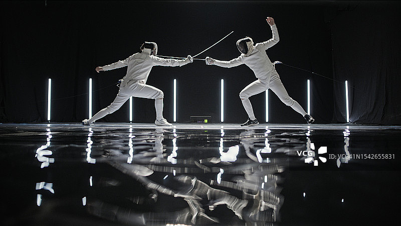 史诗舞台灯光下，两名专业击剑手进行花剑决斗图片素材
