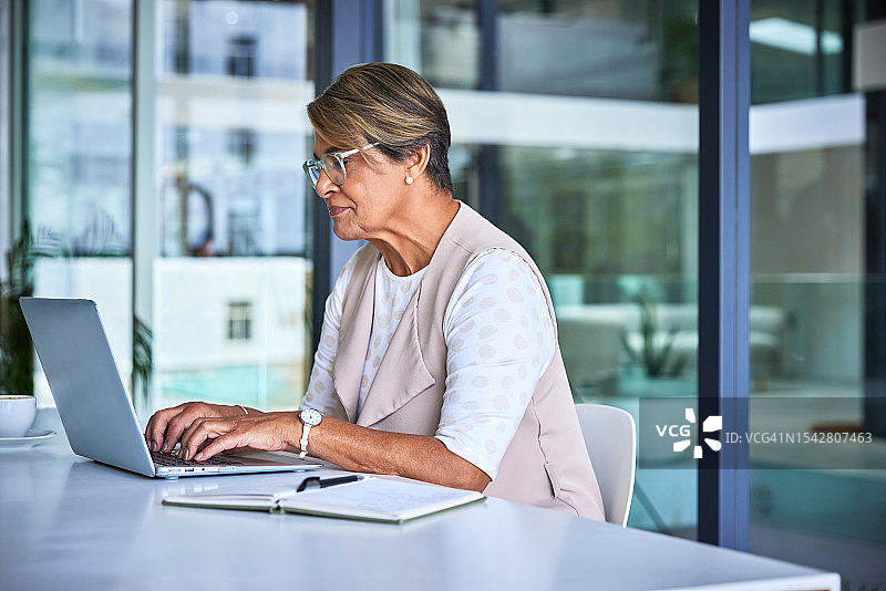 老年妇女在办公桌前用笔记本电脑打字，为办公室管理和在线安排进行研究。在互联网上，年长的接待员正在撰写行政业务报告。图片素材