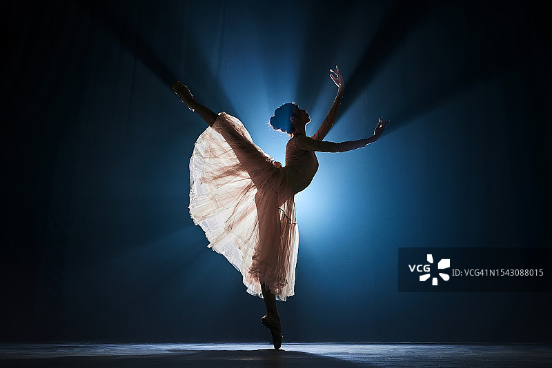 聚光灯下在深蓝色背景中跳芭蕾舞的优雅纤细才女图片素材