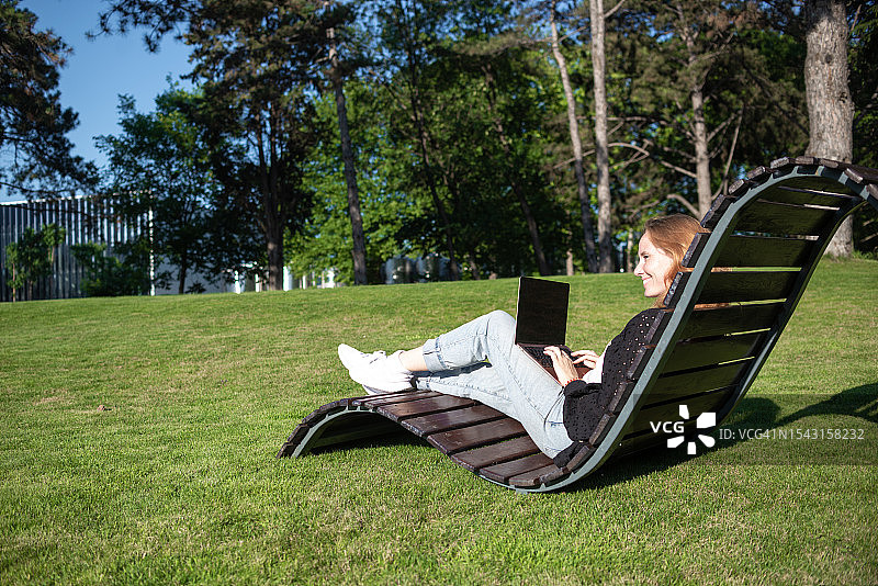 年轻女性在城市公园的背景下使用笔记本电脑图片素材