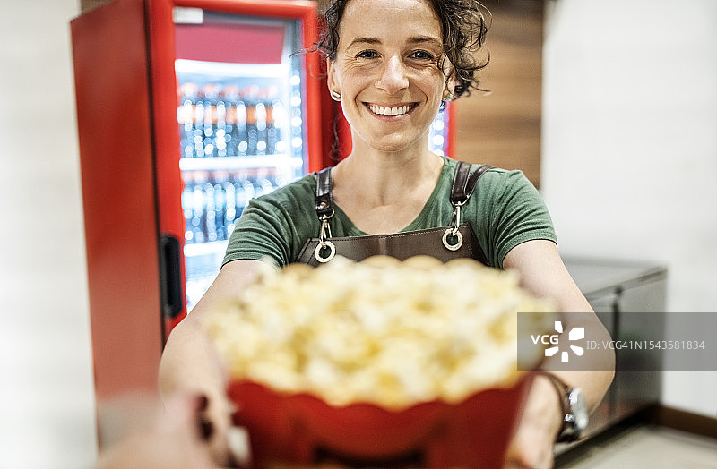 在电影院小吃摊为顾客提供爆米花的女子图片素材