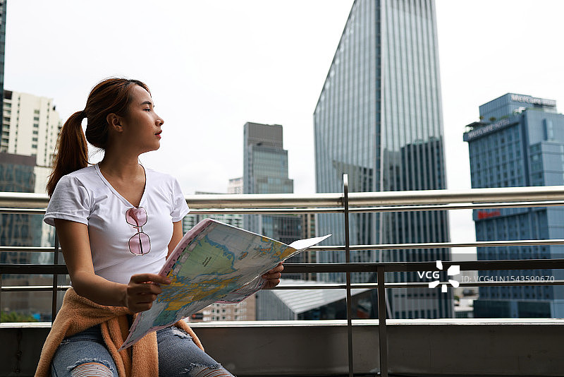 一位坐在建筑物外拿着地图的年轻女子，旅行与都市生活方式概念图片素材