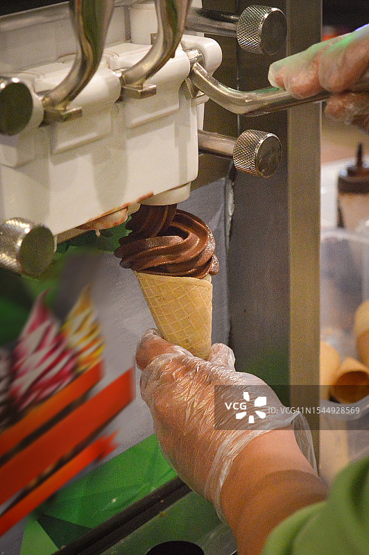 男子操作冰淇淋机，将软冰淇淋倒入蛋卷中图片素材