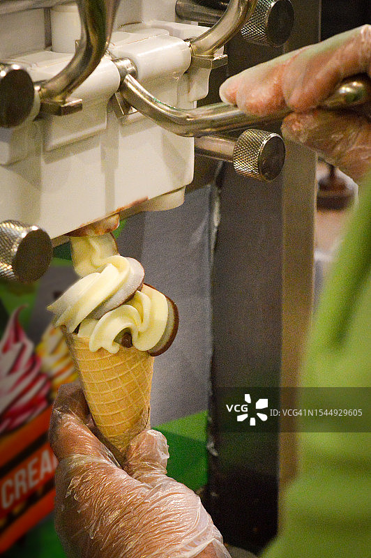 男子操作冰淇淋机，将软冰淇淋倒入蛋卷中图片素材