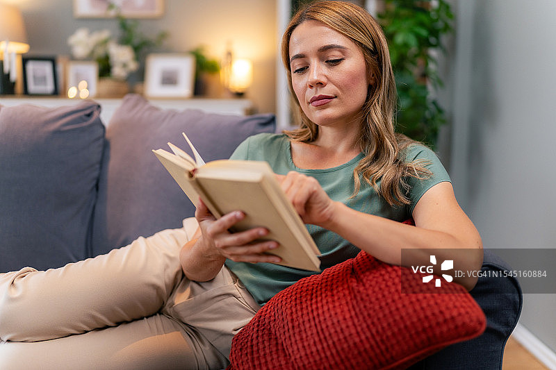 年轻女人在家里的沙发上看书图片素材