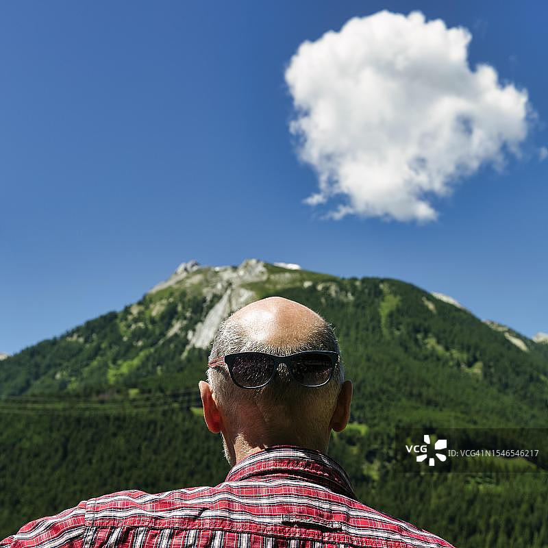 有趣的超现实肖像：秃头、戴墨镜的最佳老人，在瑞士阿尔卑斯山后方观看图片素材