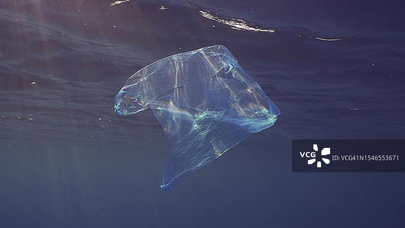 一次性蓝色塑料袋在阳光下漂浮在蓝色水面下。扔进海里的塑料袋在清晨的阳光下漂浮在蓝色水面下，红海，埃及图片素材