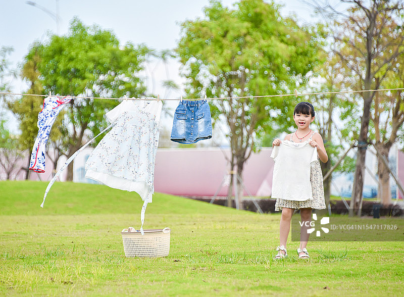 欢乐时光：在公园里微笑晾衣服的亚洲小女孩（6-7岁），中国广东省江门市图片素材