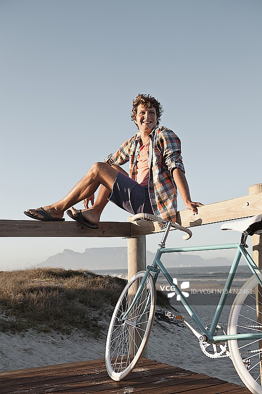 年轻男人在通往沙滩的木板路上放松图片素材