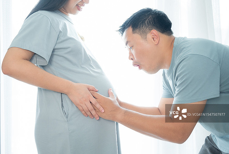 幸福的亚洲夫妇：丈夫轻抚妻子的肚子，感受宝宝的胎动图片素材