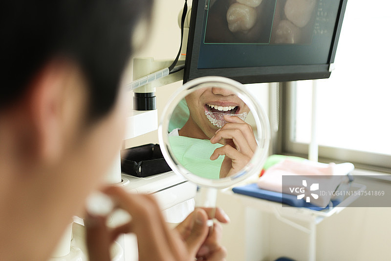 牙科诊所里，牙科助理帮助患者戴着保持器图片素材