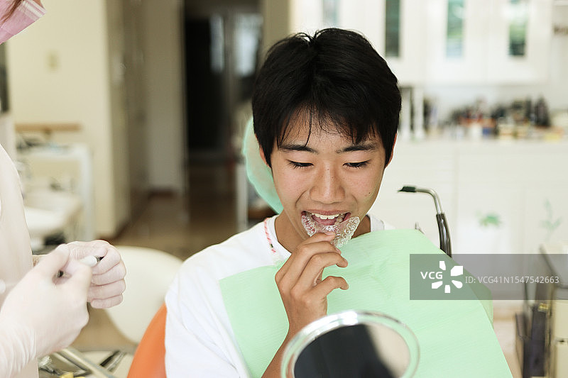 牙科诊所里，牙科助理帮助患者戴着保持器图片素材