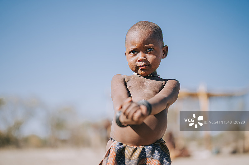 好奇的纳米比亚辛巴族男孩站在户外观看图片素材