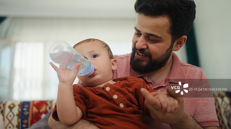 父亲在家中客厅照顾小宝宝并喂水图片素材