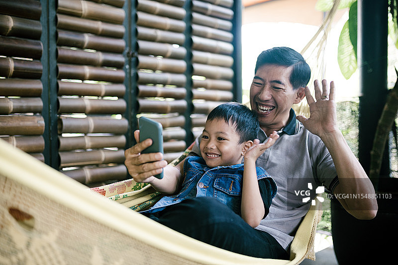 爷爷和孙子在吊床上进行视频通话图片素材