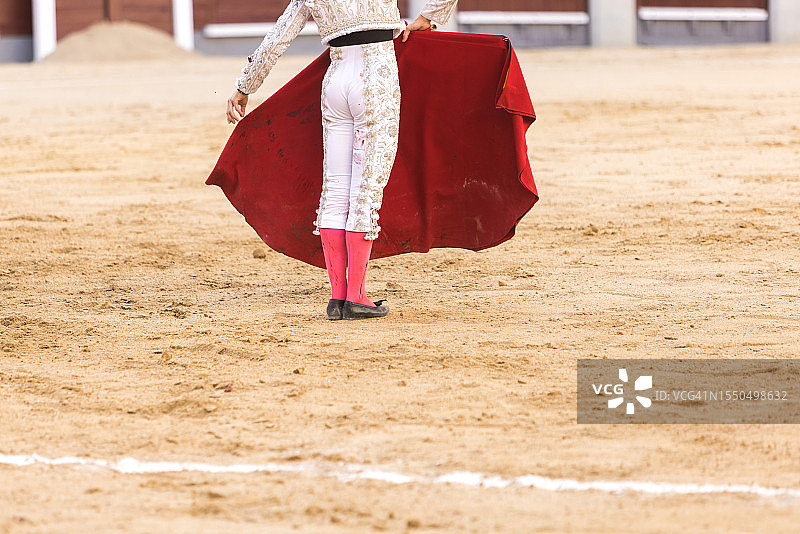 斗牛士身穿血迹斑斑的银色斗牛服，手持拐杖和细剑图片素材