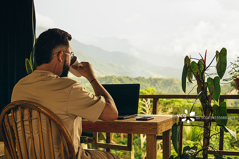 数码游民 мужчина 喝咖啡，在桌旁工作，欣赏山景图片素材