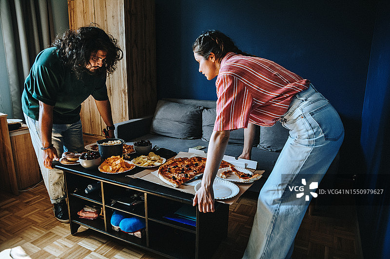 年轻夫妇准备家庭派对，备有零食和披萨图片素材