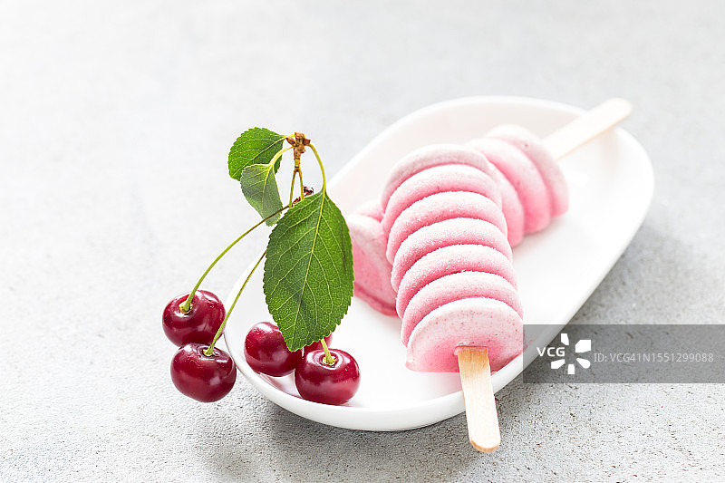 盘子里木棍上的樱桃冰淇淋，浅灰色背景特写图片素材