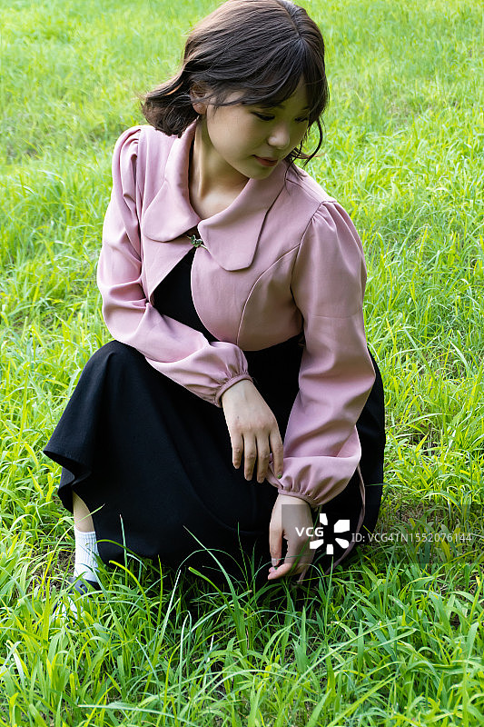 年轻漂亮的亚洲女性蹲在户外草地上，享受大自然图片素材