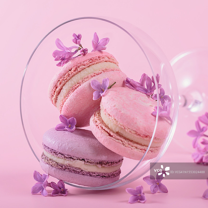 粉色背景上，玻璃高脚杯中的马卡龙和淡紫色鲜花图片素材