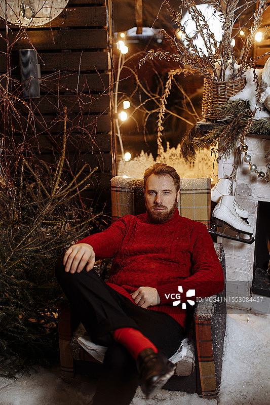 身穿红色毛衣的时尚男人坐在街边的圣诞装饰旁图片素材