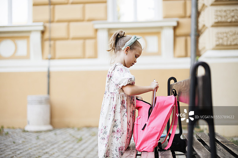 在公园长椅上整理书包的可爱女孩图片素材