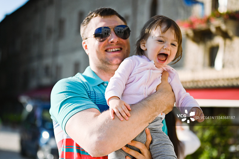 父女在户外玩耍，父亲抱着女儿在城市街道上图片素材
