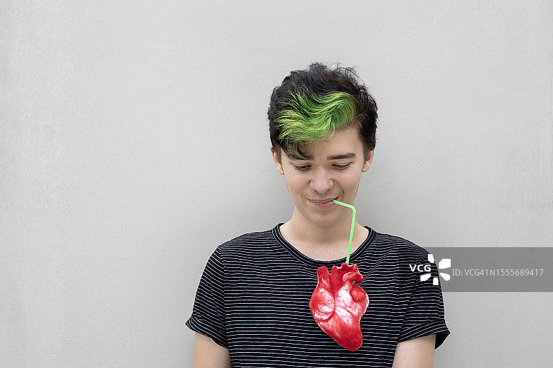 染着绿色头发的青少年男孩，手拿爱心饮品，灰色背景图片素材