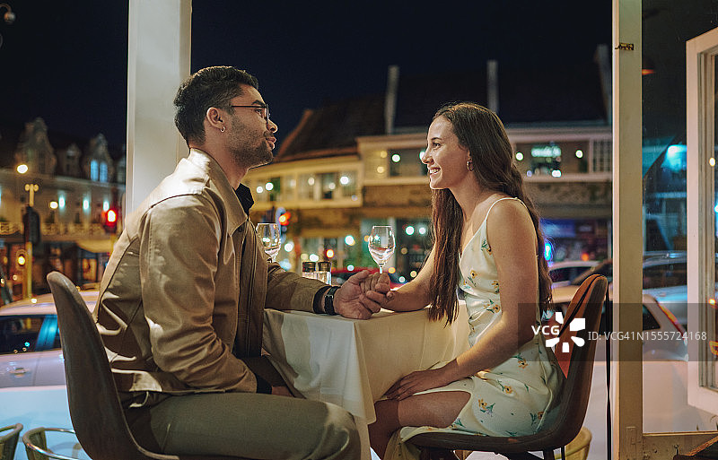 年轻情侣在晚上的晚餐约会中微笑牵手图片素材