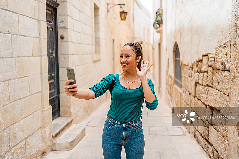 年轻女子在马耳他姆迪纳的巷子里进行视频通话图片素材