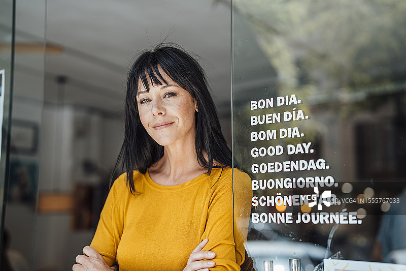 面带微笑的女人站在咖啡馆门口的玻璃旁图片素材