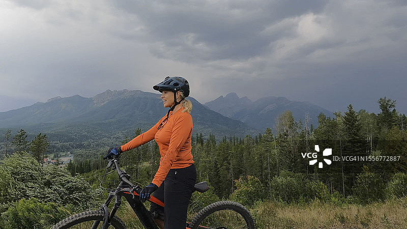 女子在森林和山脉上方骑电动山地自行车图片素材