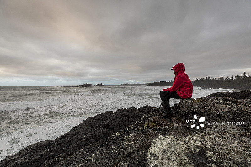 身穿红色雨衣的男孩坐在岩石上眺望大海图片素材