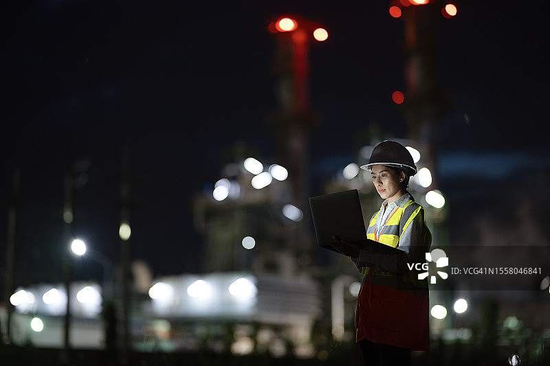 通过最大限度地减少石油和天然气能源行业的停机时间，让您从现场资产中获得最大价值的服务和维护：一名能源管理女工程师在夜班时使用笔记本电脑通过软件监控发电厂的工厂性能。图片素材