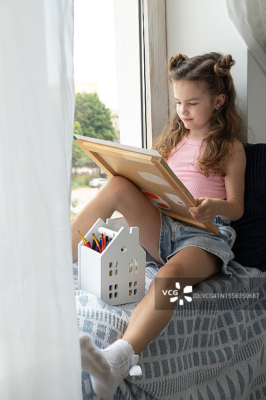 孩子坐在窗台上，在画布上用铅笔绘画图片素材