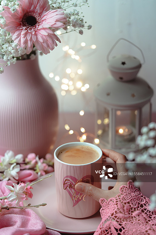 截取的女人手在桌子上的花朵旁拿着咖啡杯的特写，下午茶时光图片素材