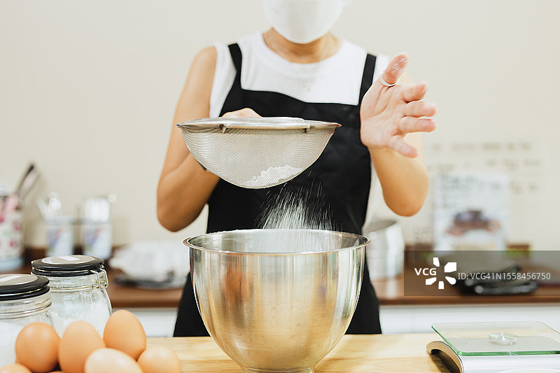 在泰国，面包师在自家厨房里将面粉筛入搅拌碗中图片素材