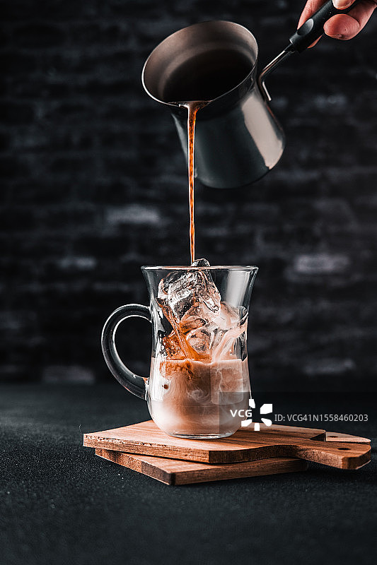 对着墙将咖啡倒入牛奶杯中的局部手部照片，乌克兰罗夫诺图片素材