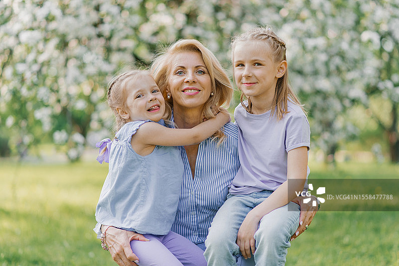 在明斯克白俄罗斯盛开的花园里，微笑的祖母拥抱她的孙女们的肖像图片素材