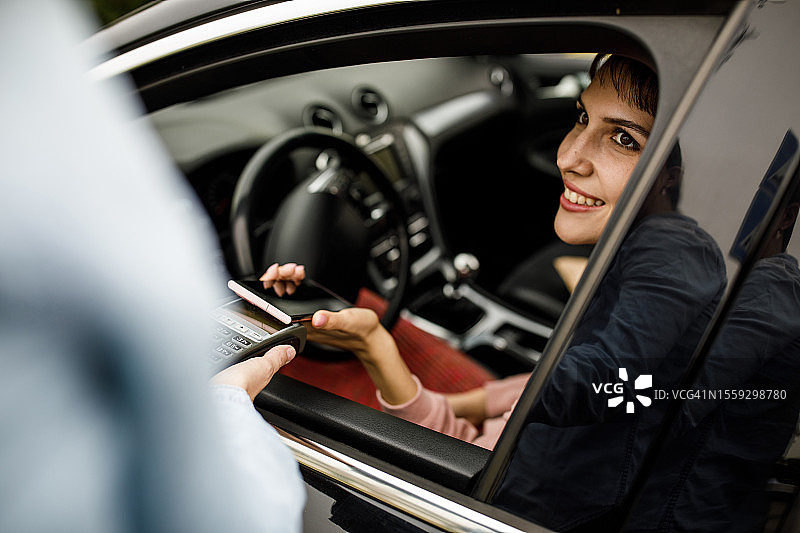 顾客坐在车里，用智能手机在路边取货处支付服务费用图片素材