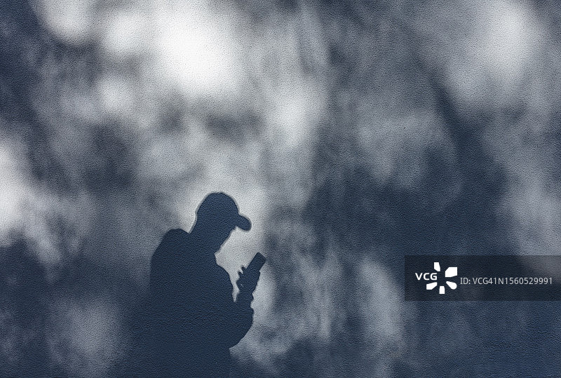 使用智能手机和戴帽子的人的影子图片素材