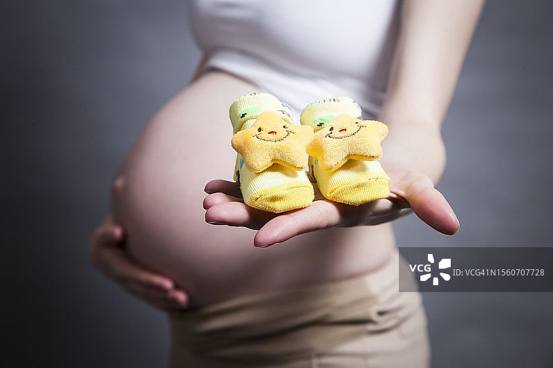 孕妇手拿婴儿鞋，黑色背景（仅身体中部）图片素材