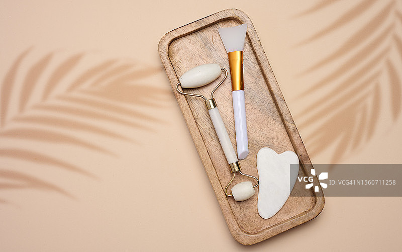 米色背景上的白玉刮痧板和按摩玉石滚轮图片素材