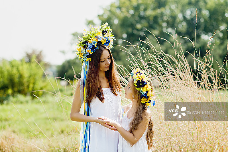 母女身穿乌克兰传统服饰，头戴蓝黄丝带花环，在田野里对视图片素材