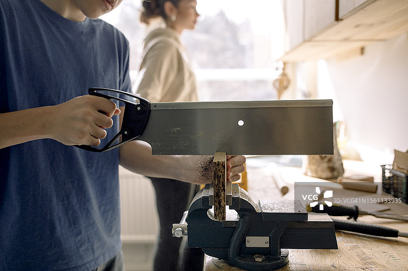 男青少年学生在木工课上用锯子锯木头的中段照片图片素材