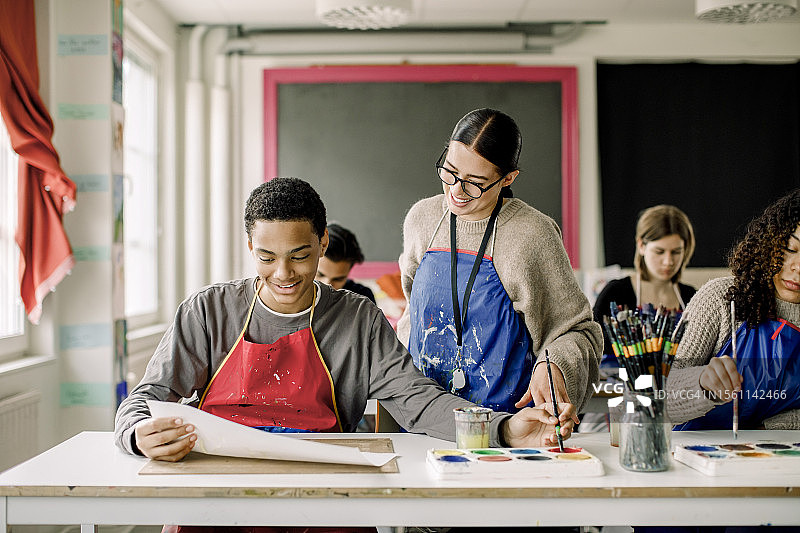 微笑的男学生在绘画课上向女老师展示画作图片素材